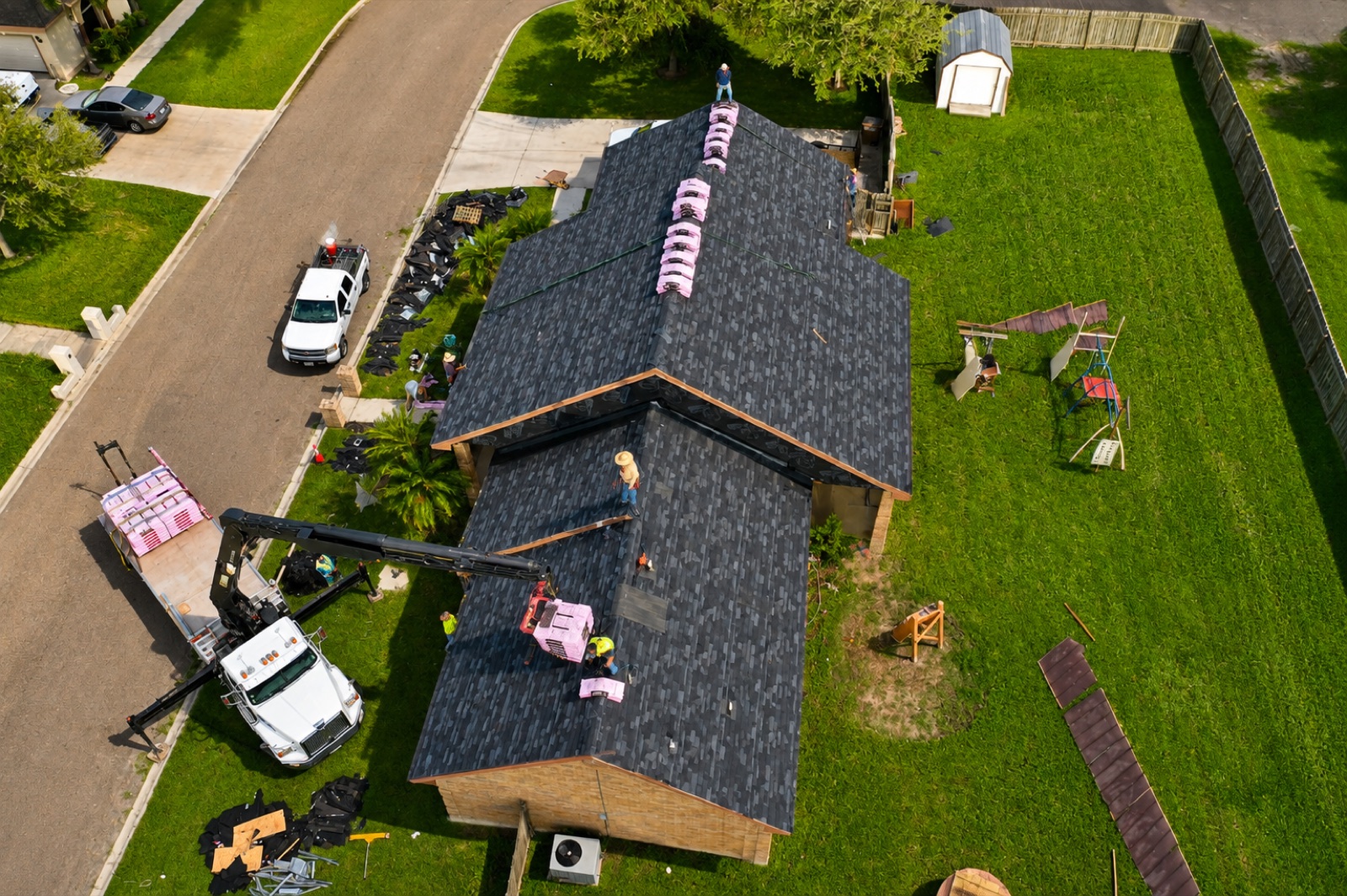 Crew installing a new shingle roof with materials staged on the roof